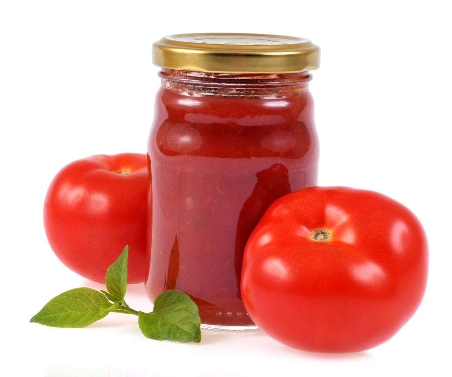 a jar of homemade tomato sauce with two fresh tomatoes and a spray of basil