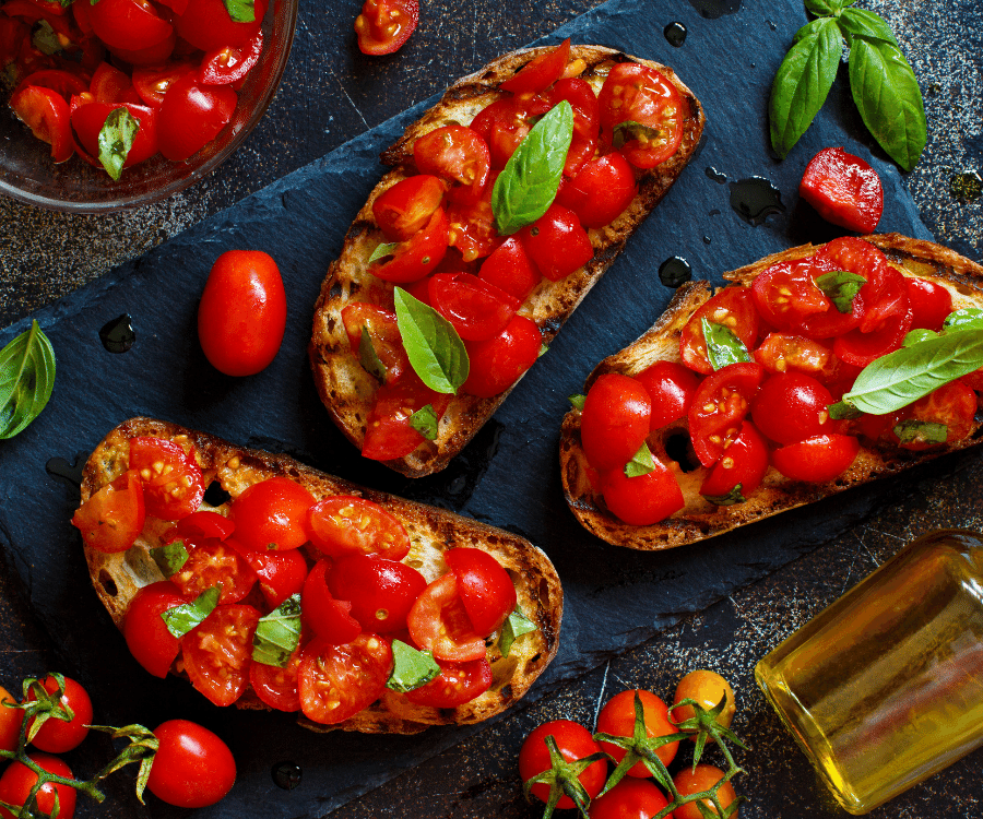 Toasts on a board topped with chopped tomato and fresh basil with a bowl of freshly chopped tomatoes to the side